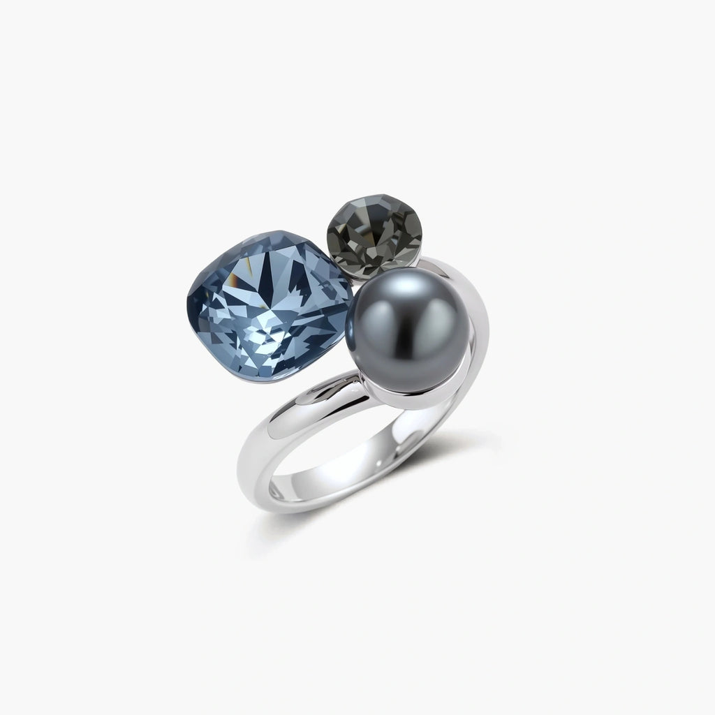 Adjustable ring with blue cushion-cut zirconia, gray pearl, and dark crystal on platinum-plated copper band against beige background.