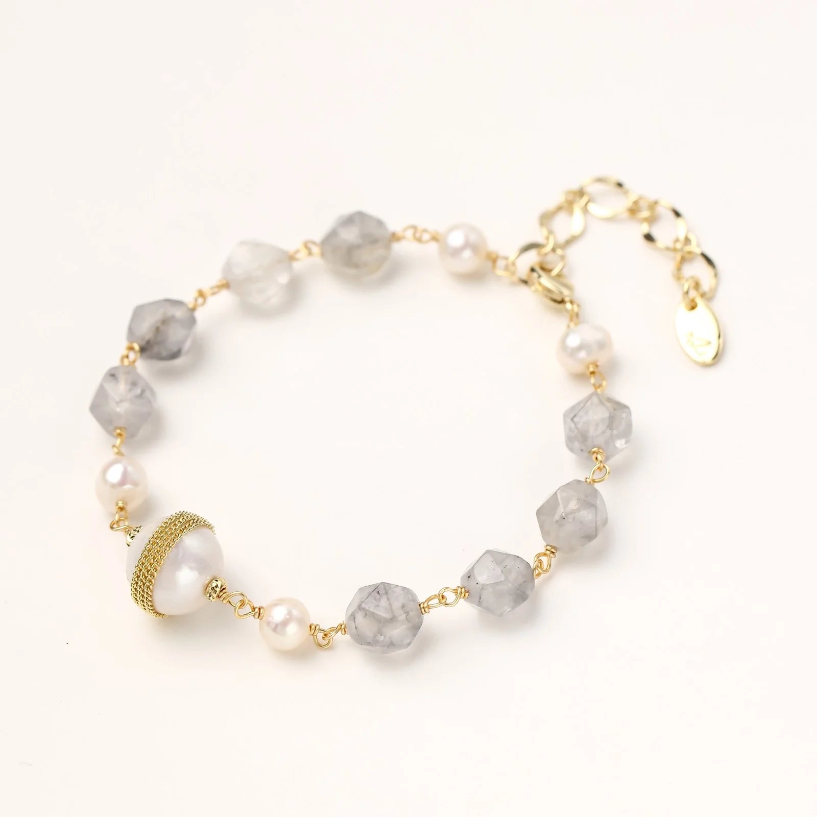 Bracelet with cloudy quartz beads, freshwater pearls, and gold-wrapped baroque pearl centerpiece on white background.