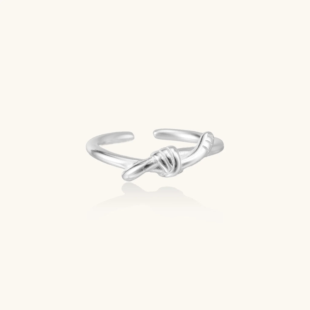 Delicate rhodium-plated silver ring with elegant knot design on cream background, adjustable band style