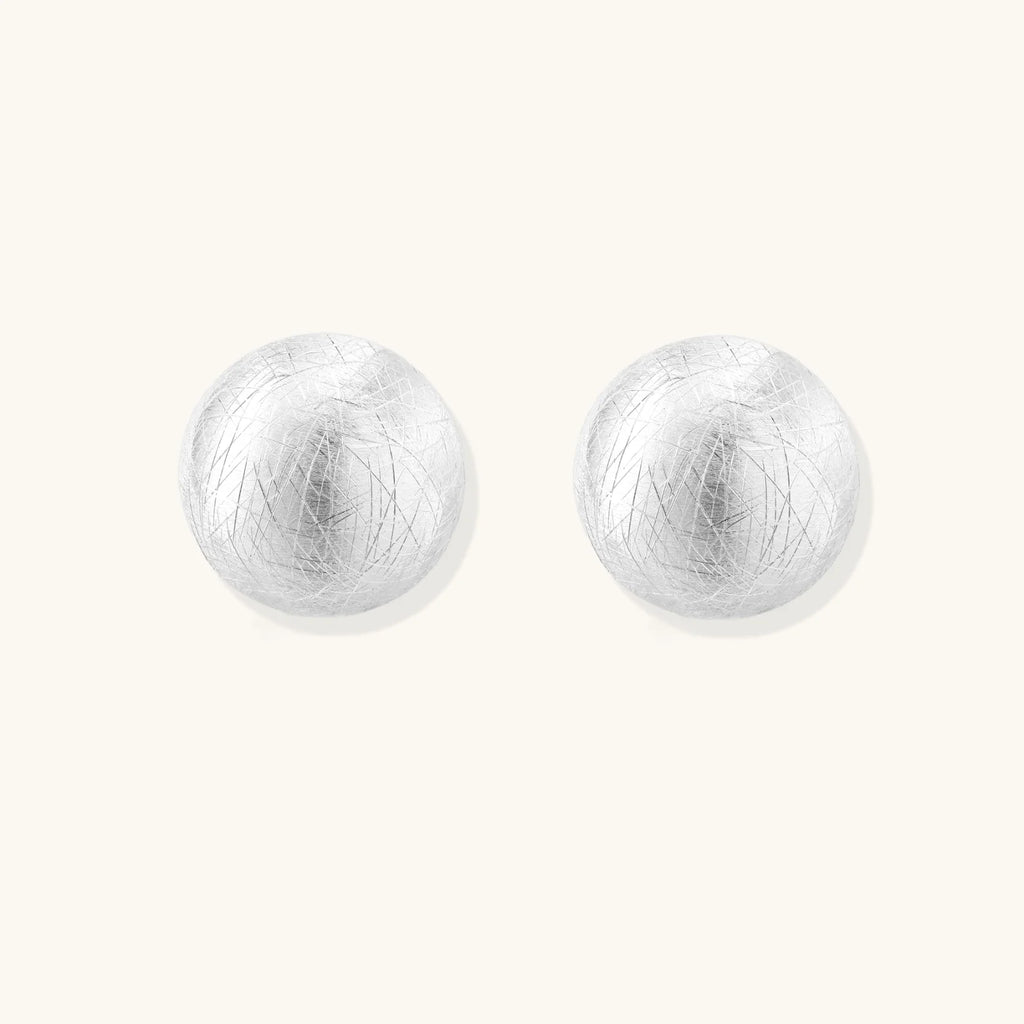 Brushed sterling silver half-dome clip-on earrings with textured surface against cream background