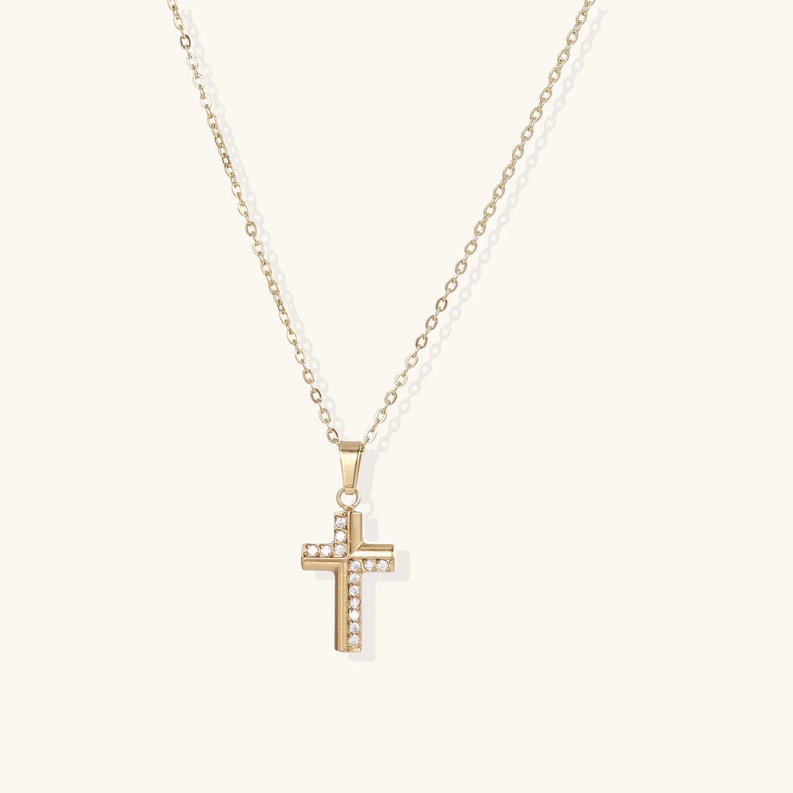 Delicate 14K gold-plated cross pendant with crystal accents on fine chain against cream background