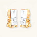Close-up of avant-garde sculptural earrings with flowing liquid metal design in gold and silver tones on white background.