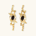 Elongated sculptural earrings with organic openwork design in eco-zinc alloy and dark resin accents on white background.
