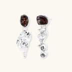 Abstract sculptural silver earrings with brown resin stones featuring organic fluid metalwork design on white background.