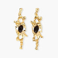 Elongated sculptural earrings with organic openwork design in eco-zinc alloy and dark resin accents on white background.