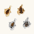 Sculptural gold-tone earrings with flowing organic forms and amber gemstone accents on neutral background