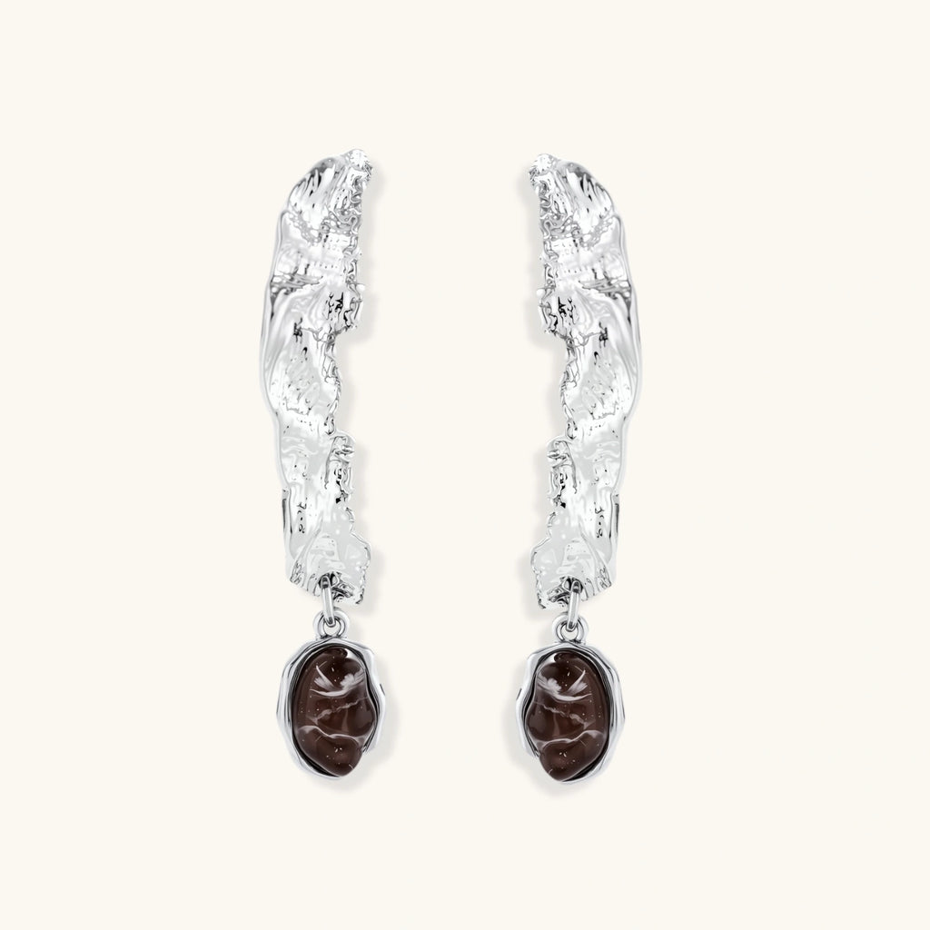 Silver-toned twisted metal earrings with dark brown oval resin stones dangling from sculptural posts on white background.