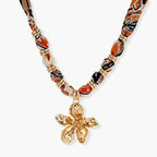 Vibrant patterned fabric necklace with gold-toned flower pendant featuring rhinestone center on white background