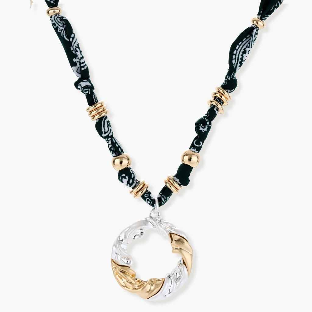 Adjustable necklace with black paisley fabric cord, gold metal spacers, and clear twisted pendant on cream background