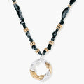 Adjustable necklace with black paisley fabric cord, gold metal spacers, and clear twisted pendant on cream background