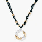 Adjustable necklace with black paisley fabric cord, gold metal spacers, and clear twisted pendant on cream background