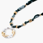Adjustable necklace with black paisley fabric cord, gold metal spacers, and clear twisted pendant on cream background