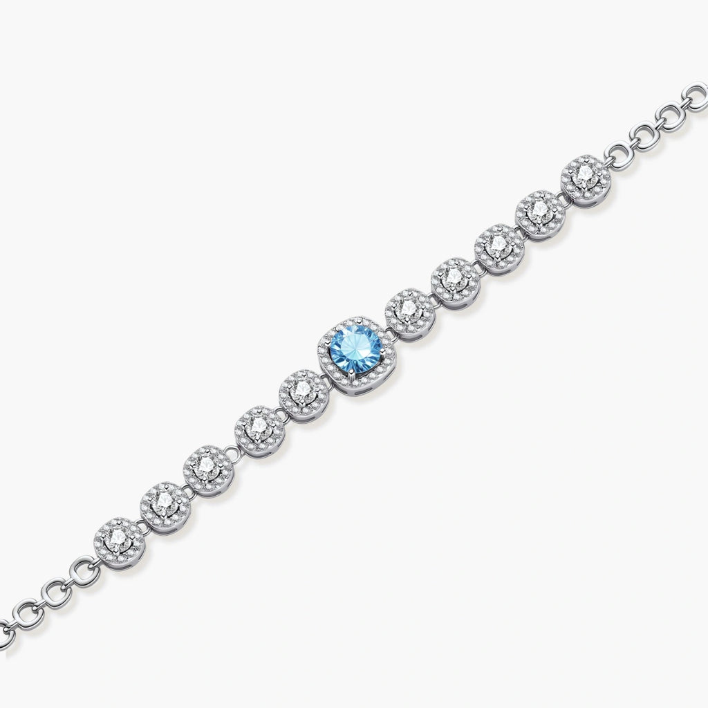 Sterling silver tennis bracelet with round halo-set moissanite stones and blue center stone on cream background.