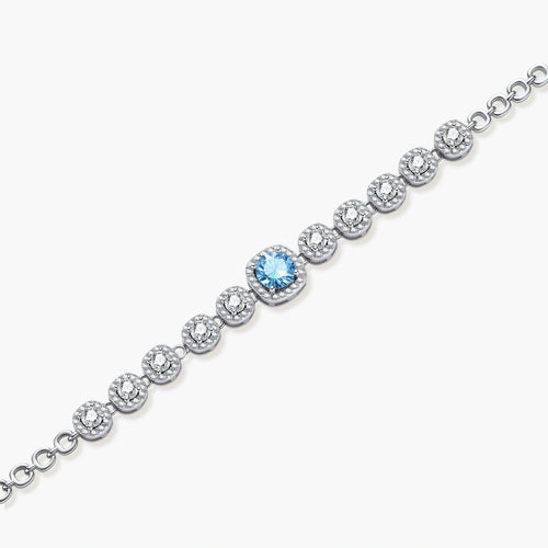 Sterling silver tennis bracelet with round halo-set moissanite stones and blue center stone on cream background.