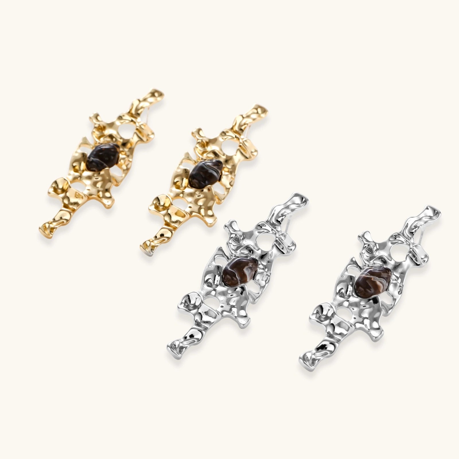 Gold-toned abstract dangle earrings with flowing cutout design and dark resin center accents on white background.