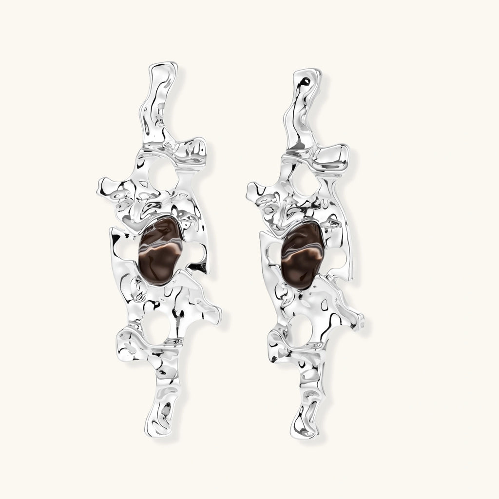 Flowing silver-toned earrings with organic liquid shapes and embedded brown resin stones on white background.