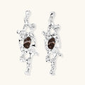 Flowing silver-toned earrings with organic liquid shapes and embedded brown resin stones on white background.