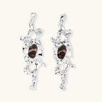 Flowing silver-toned earrings with organic liquid shapes and embedded brown resin stones on white background.