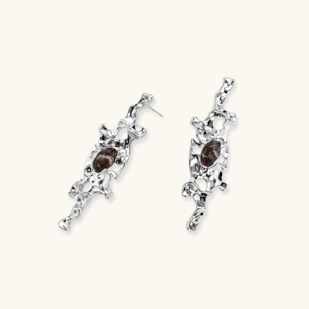 Flowing silver-toned earrings with organic liquid shapes and embedded brown resin stones on white background.