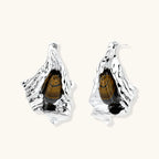 Silver sculptural earrings with flowing molten forms and amber gemstones, featuring 925 silver posts on white background.