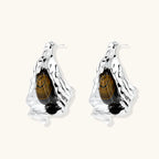 Silver sculptural earrings with flowing molten forms and amber gemstones, featuring 925 silver posts on white background.