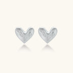 Pair of brushed platinum-plated 925 sterling silver puffy heart stud earrings on a cream background.