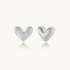 Pair of brushed platinum-plated 925 sterling silver puffy heart stud earrings on a cream background.
