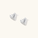 Pair of brushed platinum-plated 925 sterling silver puffy heart stud earrings on a cream background.