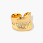 Adjustable gold-plated cuff ring with parallel ridged texture and diagonal row of sparkling zirconia stones on white background.